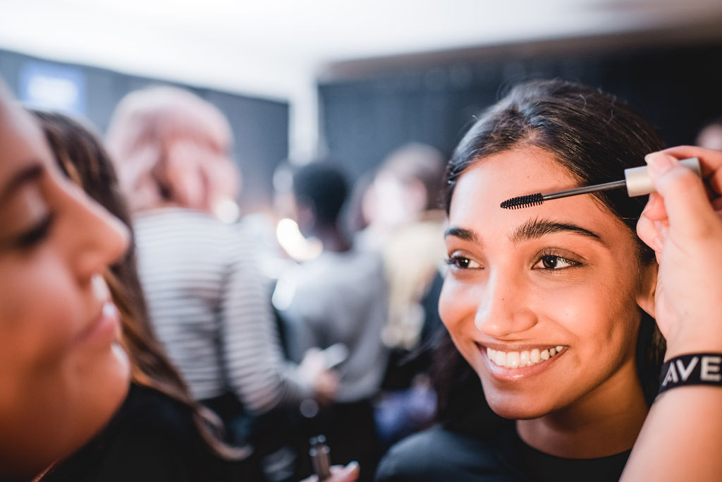 Esthetics/Makeup Artist applying mascara to smiling student